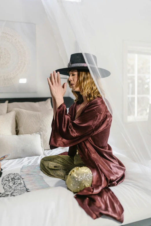 a man sitting on top of a bed next to a woman, by Sara Saftleven, trending on pexels, silk hat, doing a sassy pose, casting a protection spell, maroon hat