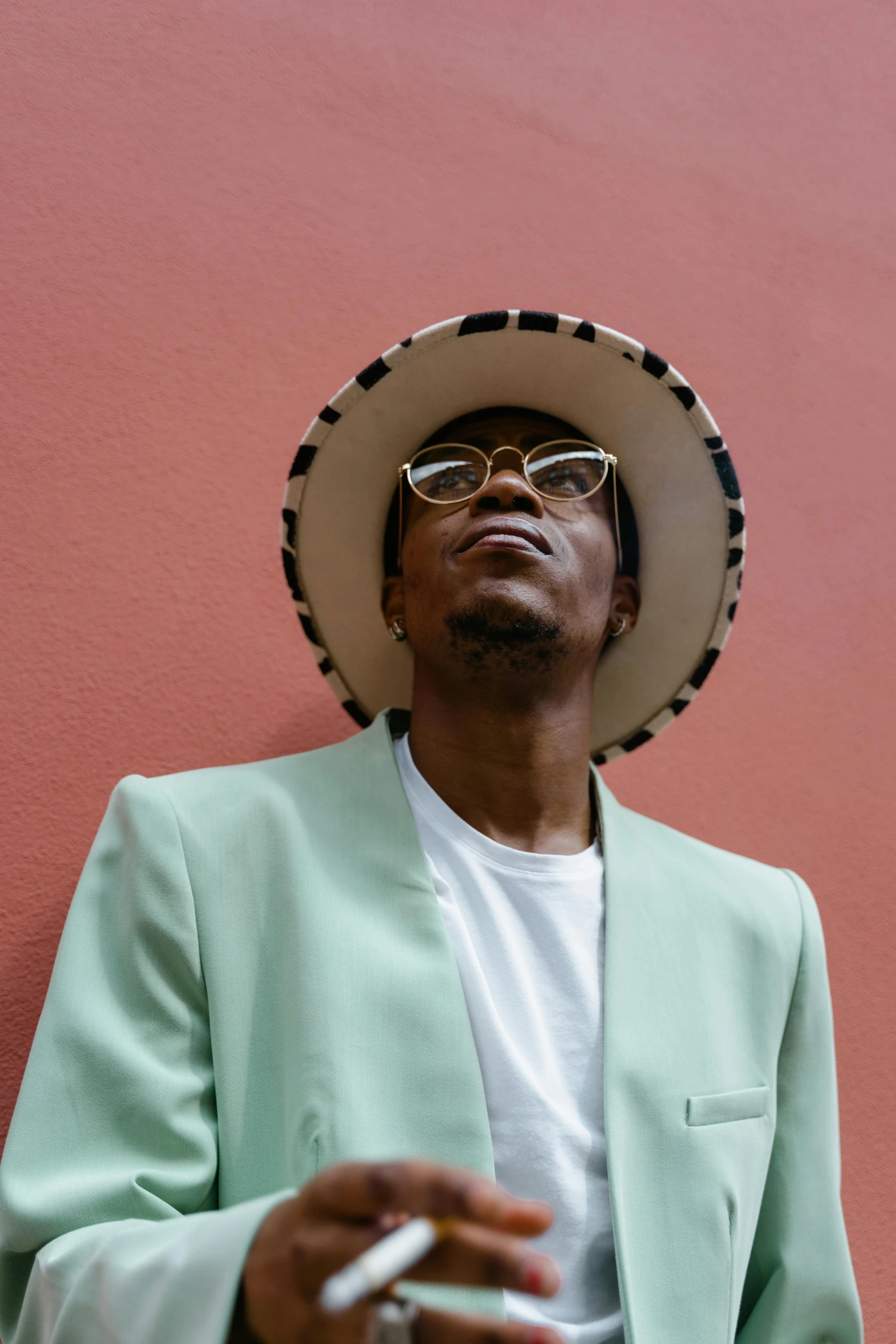 a man wearing a hat and holding a cigarette, an album cover, trending on pexels, afrofuturism, wearing white suit and glasses, sea - green and white clothes, androgynous person, julian ope