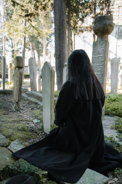a woman in a black robe sitting in a cemetery, unsplash, with his back turned, female with long black hair, ( ( theatrical ) ), ignant