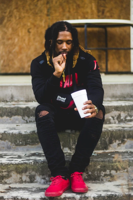 a man sitting on the steps of a building, an album cover, trending on pexels, visual art, holding a drink, full body black and red longcoat, dreads, thoughtful )