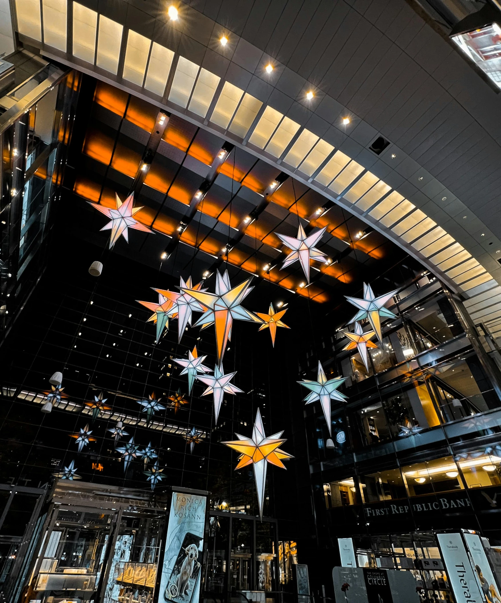 a bunch of stars hanging from the ceiling of a building, with shiny glass buildings, fully decorated, front facing, tyndall rays