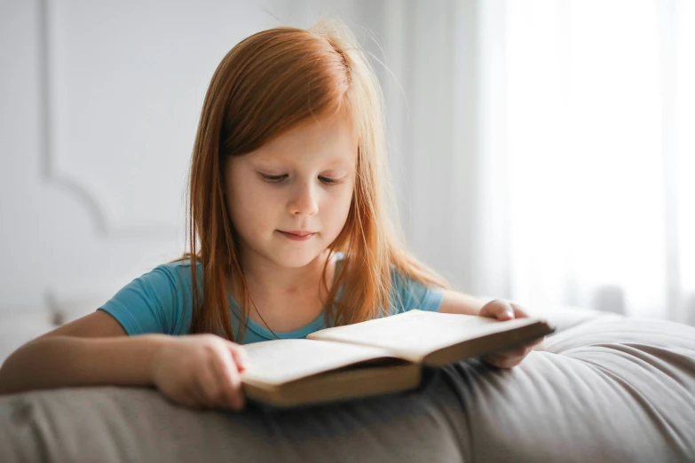 a little girl reading a book on a couch, pexels contest winner, figuration libre, ginger hair with freckles, school curriculum expert, girl wearing uniform, bedhead