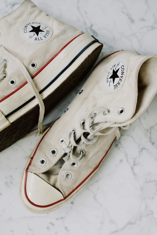 a pair of white sneakers sitting on top of a marble floor, a colorized photo, trending on pexels, converse, beige, 1970's, plain background