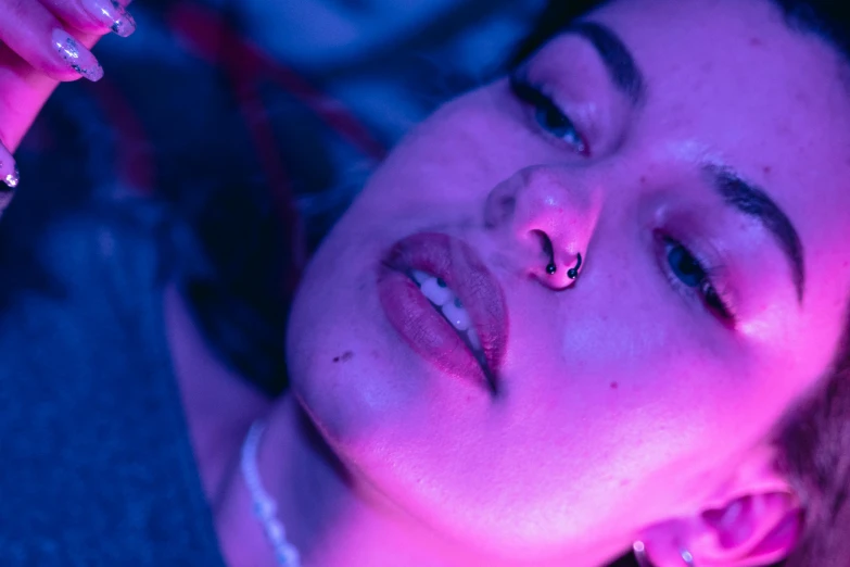 a close up of a person holding a cell phone, an album cover, inspired by Elsa Bleda, massurrealism, blue lights and purple lights, nose ring, laying down, official music video