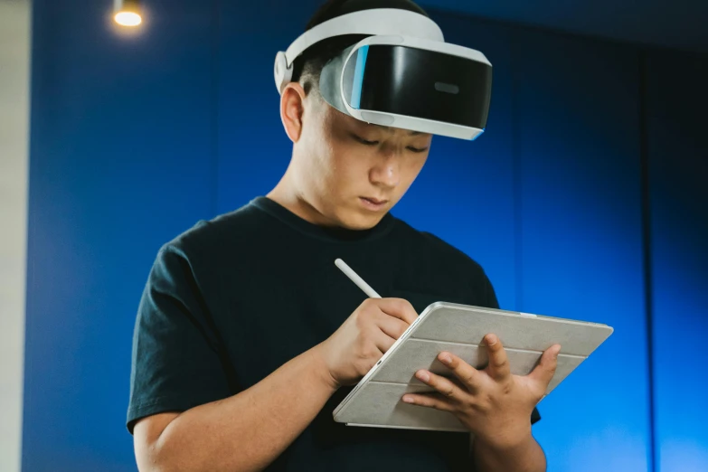 a man wearing a virtual reality headset and writing on a tablet, inspired by Zhu Da, pexels contest winner, hyperrealism, sleek blue visor for eyes, a person standing in front of a, bao pham, johnson ting