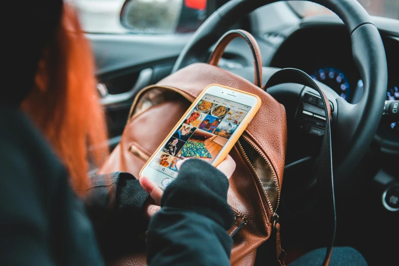 a person sitting in a car holding a cell phone, a picture, by Julia Pishtar, trending on pexels, happening, carrying a saddle bag, long orange sweatshirt, 🦩🪐🐞👩🏻🦳, schools