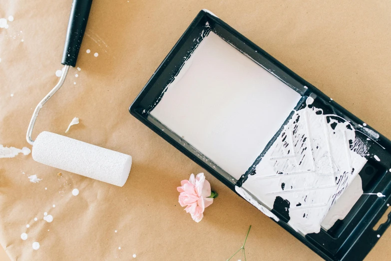 a piece of paper sitting on top of a table next to a paint roller, by Julia Pishtar, unsplash, action painting, white powder makeup, white box, white and black, on a wooden tray