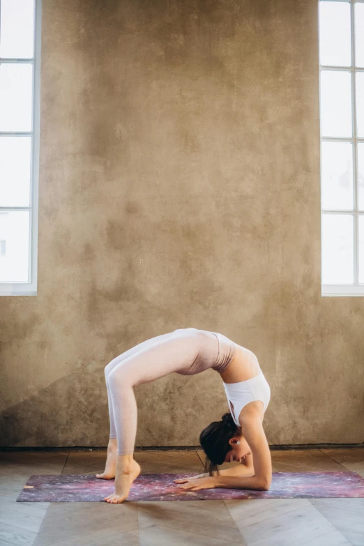 a woman doing a handstand pose on a yoga mat, a picture, by Arabella Rankin, pexels contest winner, arabesque, white sweeping arches, high arched ceiling, vintage glow, gif