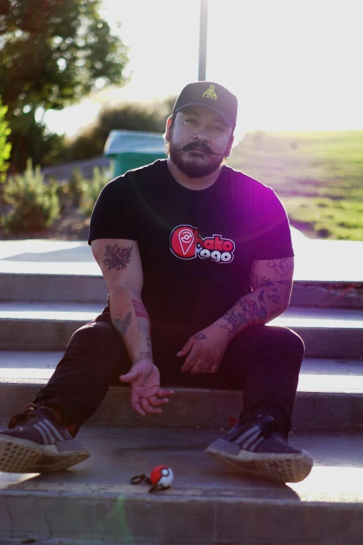 a man sitting on some steps with a skateboard, a tattoo, inspired by Randy Gallegos, lyco art, wearing a black tshirt, jontron, panoramic shot, mexican mustache