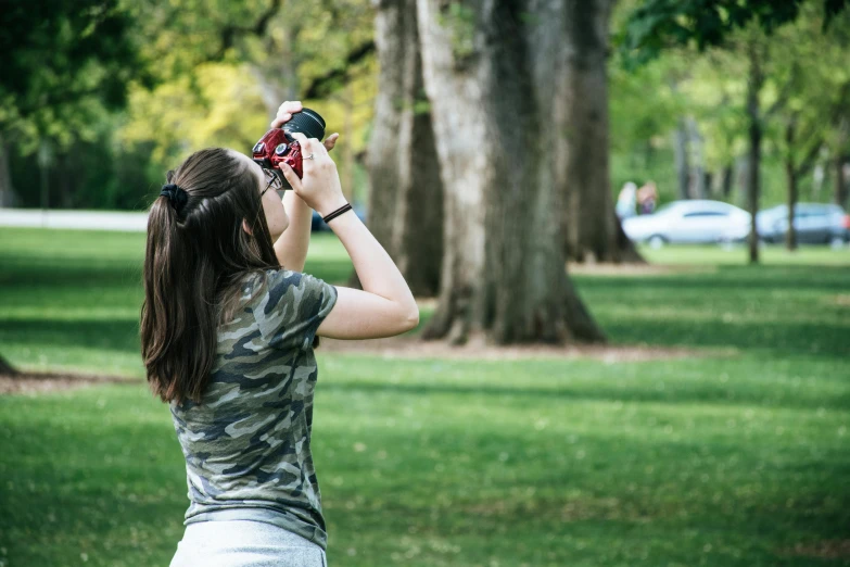 a woman taking a picture of a tree in a park, a picture, pexels contest winner, over the shoulder, holding a camera, low iso, college