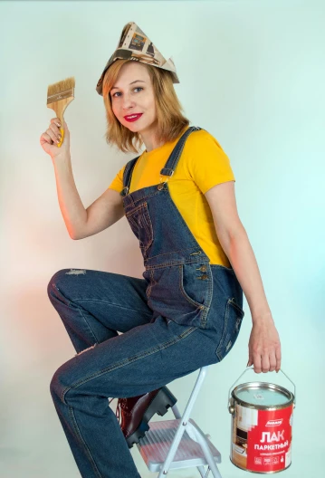a woman sitting on a chair holding a paint brush, inspired by Norman Rockwell, trending on pexels, arbeitsrat für kunst, wearing blue jean overalls, lady using yellow dress, attractive photo, cute girl wearing tank suit