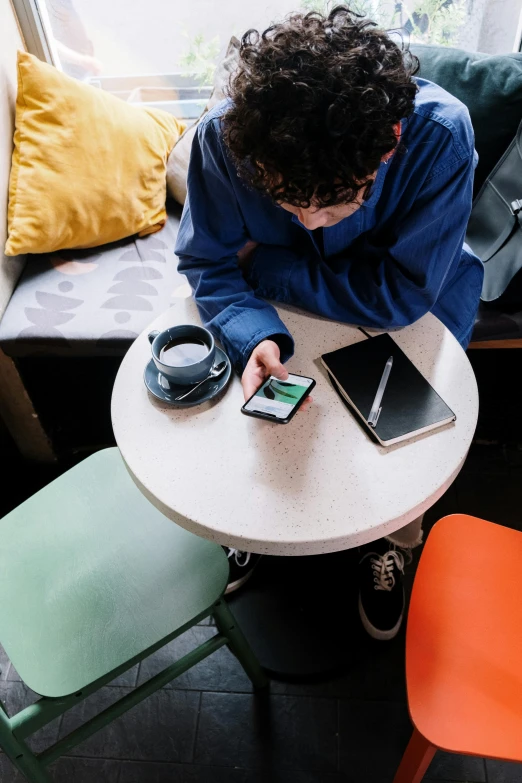 a person sitting at a table using a cell phone, colour photo, schools, coffee, round format