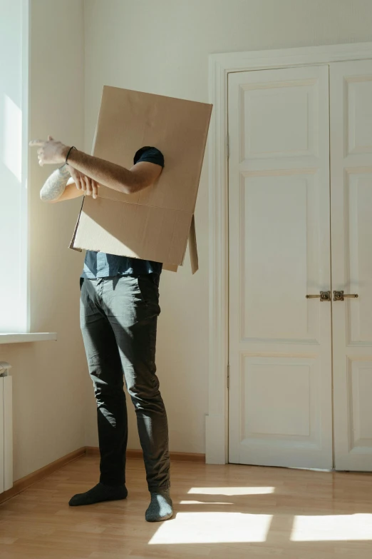 a man standing in a room holding a cardboard box, pexels contest winner, conceptual art, humanoid shape, costume, baggy, afternoon