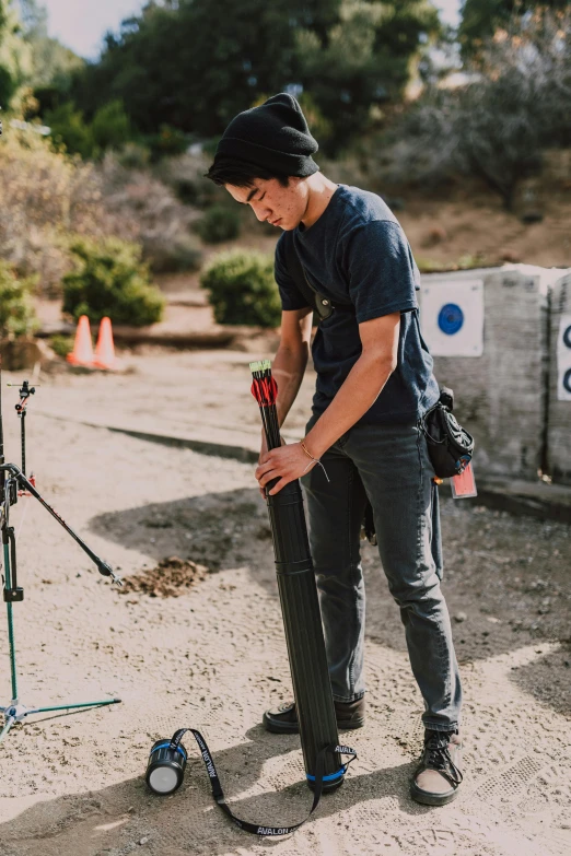 a man standing next to a camera on a tripod, wearing cargo pants, holding a staff, jc park, holding a rocket