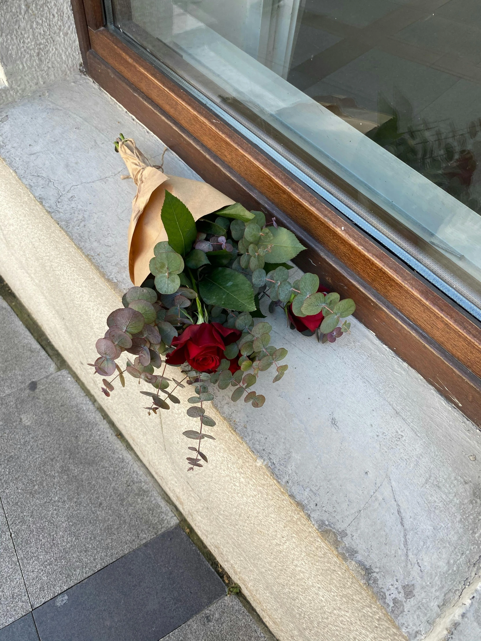 a bouquet of flowers sitting on the ledge of a window sill, on the sidewalk, holding a red rose, payne's grey and venetian red, wrapped