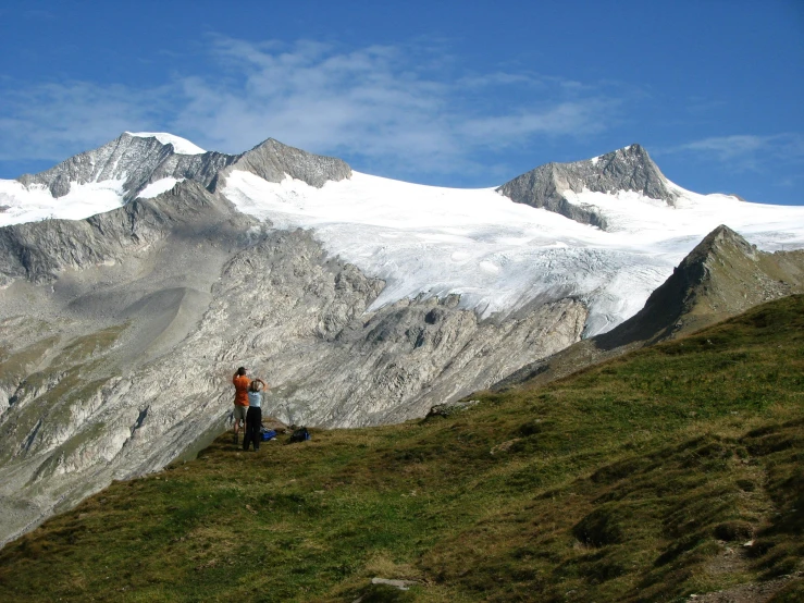 a man standing on top of a lush green hillside, a photo, inspired by Werner Andermatt, glaciers and ice and snow, two mountains in background, humans exploring, slide show