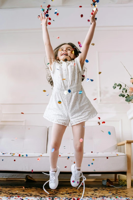 a little girl jumping in the air with confetti, happening, wearing white pajamas, on a white table, gen z, may)