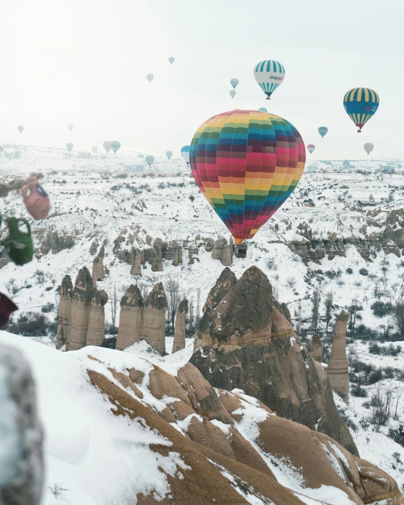 a group of hot air balloons flying over a snow covered mountain, a colorized photo, pexels contest winner, photo for vogue, muted rainbow tubing, mittens, holiday