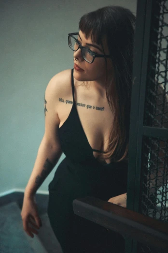 a woman in a black dress posing for a picture, a tattoo, inspired by Elsa Bleda, reddit, glasses, 33mm photo, roleplay, indoor picture