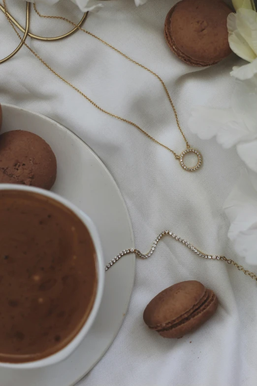 a cup of coffee and some macaroons on a table, by Nina Hamnett, gold necklace, close up details, circle, diamond chain