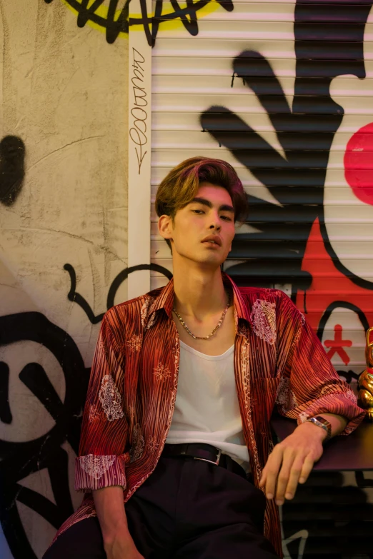 a man sitting in front of a graffiti covered wall, an album cover, trending on pexels, cai xukun, 8 0 s asian neon movie still, young greek man, zayn malik