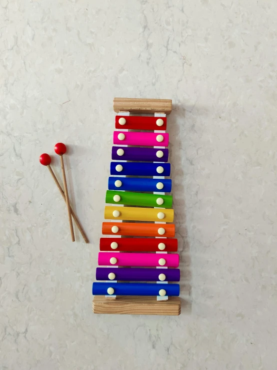 a colorful xylophone sitting next to a matchstick, inspired by Jan Rustem, flat lay, tall, multicoloured, bells