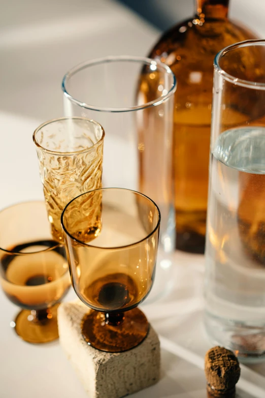 a couple of glasses sitting on top of a table, a still life, unsplash, renaissance, liquid translucent amber, understated, detailed product shot, various sizes