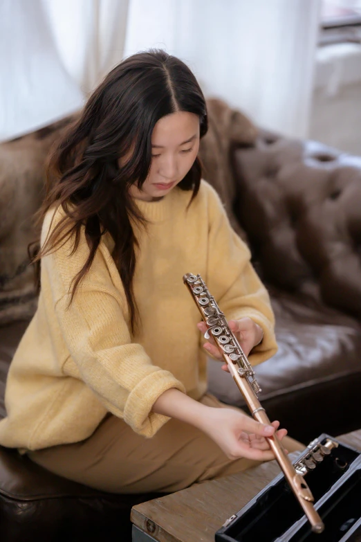 a woman sitting on a couch playing a flute, inspired by Li Di, trending on pexels, sweater, yanjun chengt, brown, gold