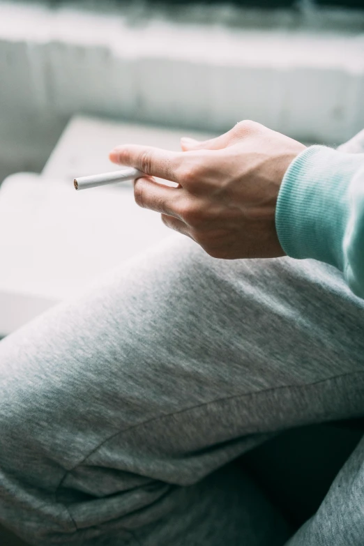 a person sitting on a couch with a cigarette in their hand, fine point pen, wearing a hoodie and sweatpants, diary on her hand, 2019 trending photo