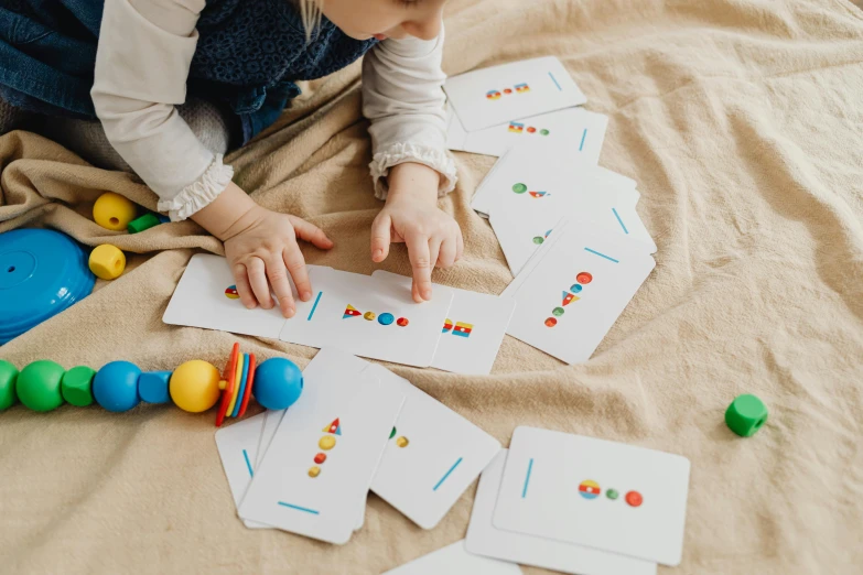 a little girl that is playing with some cards, by Emma Andijewska, pexels contest winner, floating spheres and shapes, vinyl designer toy, pair of keycards on table, card template