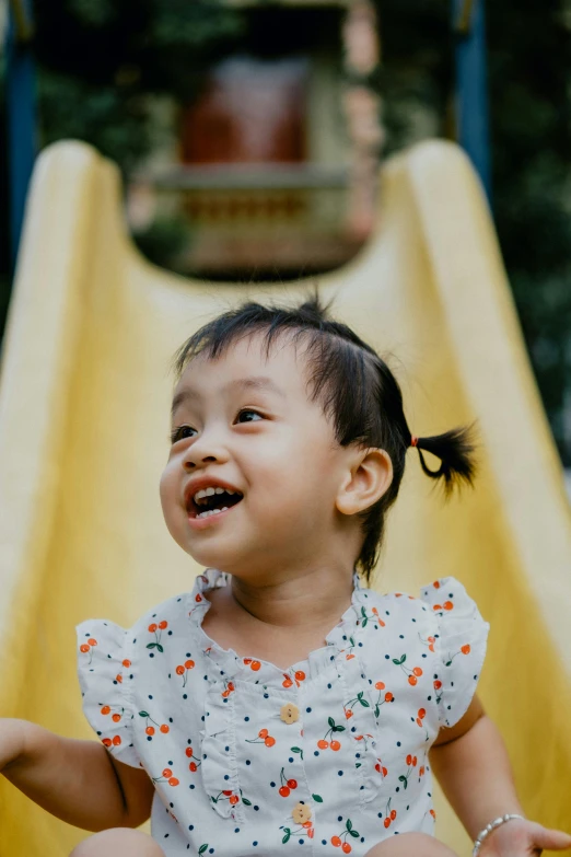 a little girl sitting on top of a yellow slide, pexels contest winner, jakarta, turning her head and smiling, at a park, toddler