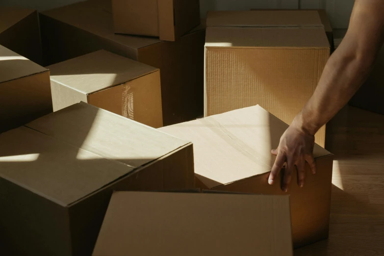 a person reaching for a box in a room full of boxes, by Carey Morris, pexels contest winner, hurufiyya, sydney hanson, slightly tanned, afternoon sun, background image