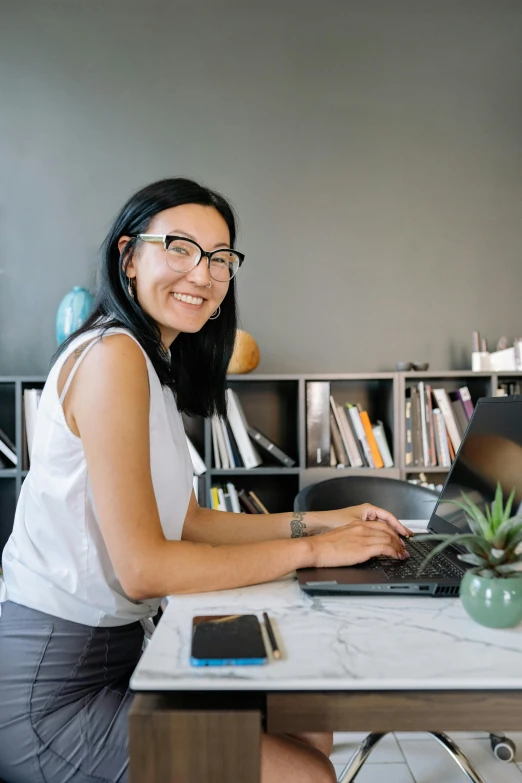 a woman sitting at a desk using a laptop computer, inspired by Ruth Jên, pexels contest winner, happening, smiling into the camera, cute slightly nerdy smile, avatar image, professional profile picture