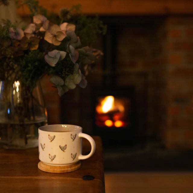 a coffee cup sitting on top of a wooden table, a still life, by Alice Mason, pexels contest winner, arts and crafts movement, cosy fireplace, fireflys, cottagecore, shot on 85mm