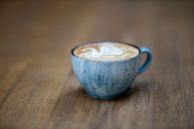 a close up of a cup of coffee on a table, by Nick Fudge, unsplash, photorealism, soft blue texture, on wood, brown, milk