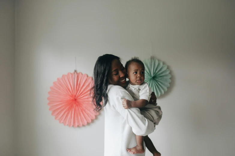 a woman holding a baby in her arms, a picture, by Arabella Rankin, pexels contest winner, hurufiyya, in front of white back drop, decoration, fan favorite, riyahd cassiem