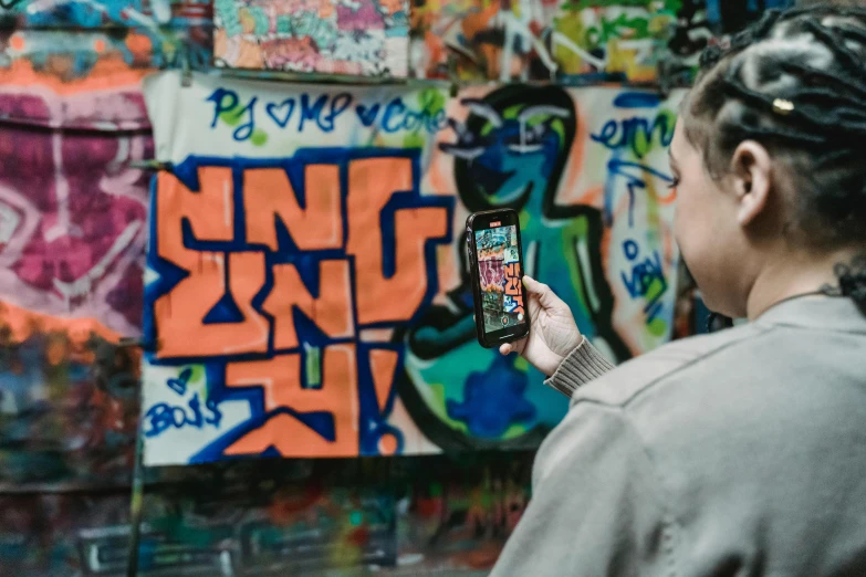 a woman standing in front of a wall covered in graffiti, pexels contest winner, a painting of an iphone, on a canva, performing, digital screens on the walls