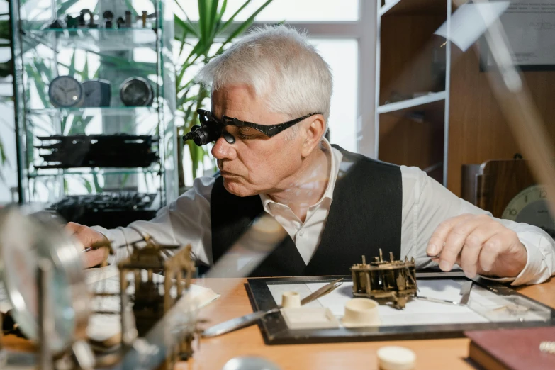 a man sitting at a table working on a piece of art, by Adam Marczyński, pexels contest winner, steampunk glasses, frank gehry, foxish guy in a lab coat, aged armor plating