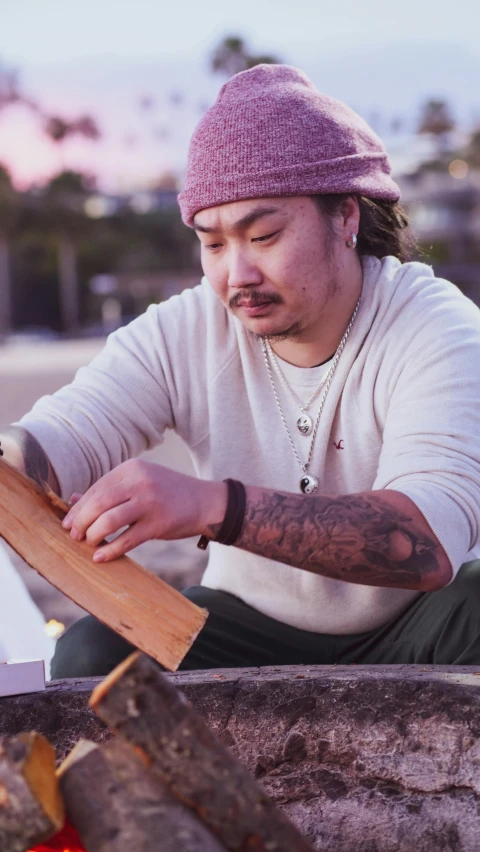 a man that is sitting in front of a fire, an album cover, trending on unsplash, ukiyo-e, holding a wood piece, chris chan, drawing sketches on his notebook, skateboard art