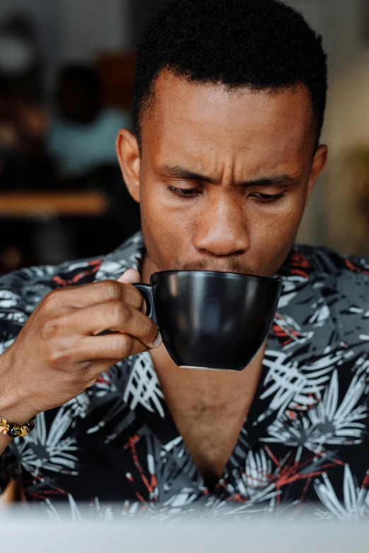 a man sitting at a table with a cup of coffee, smelling good, wearing a black shirt, patterned, dark-skinned