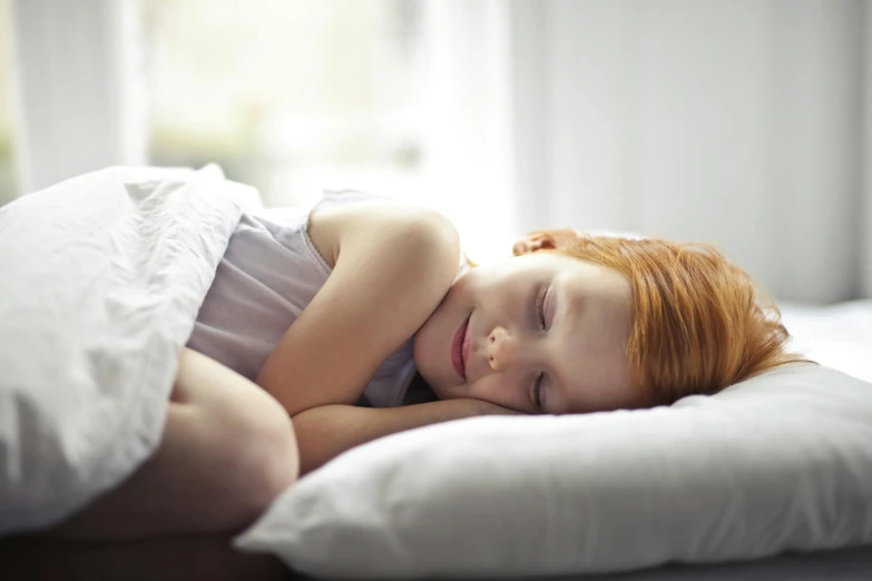 a little girl laying on top of a pillow on a bed, by Elizabeth Durack, pexels, woman with red hair, asleep, smiling, ad image