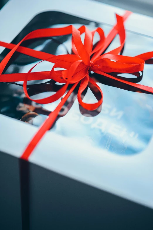 a white box with a red ribbon wrapped around it, pexels contest winner, glossy surface, **cinematic, front lit, seasonal