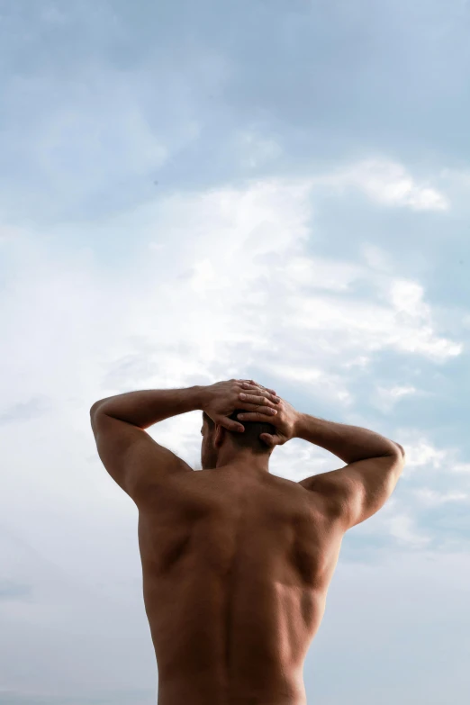 a man standing on top of a beach next to the ocean, a statue, bare back, defined muscles, looking at the sky, 2019 trending photo