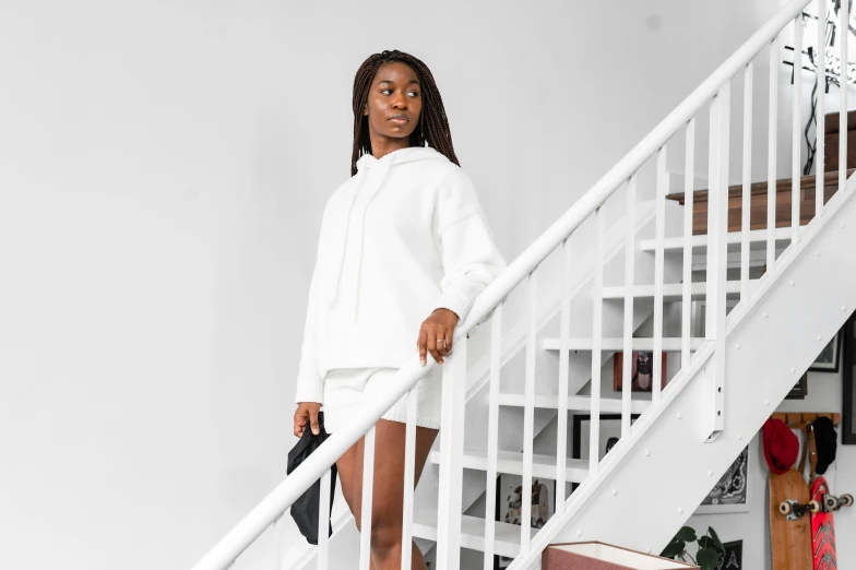 a woman standing at the top of a set of stairs, happening, oversized hoodie, wearing white skirt, wearing nanotech honeycomb robe, young black woman