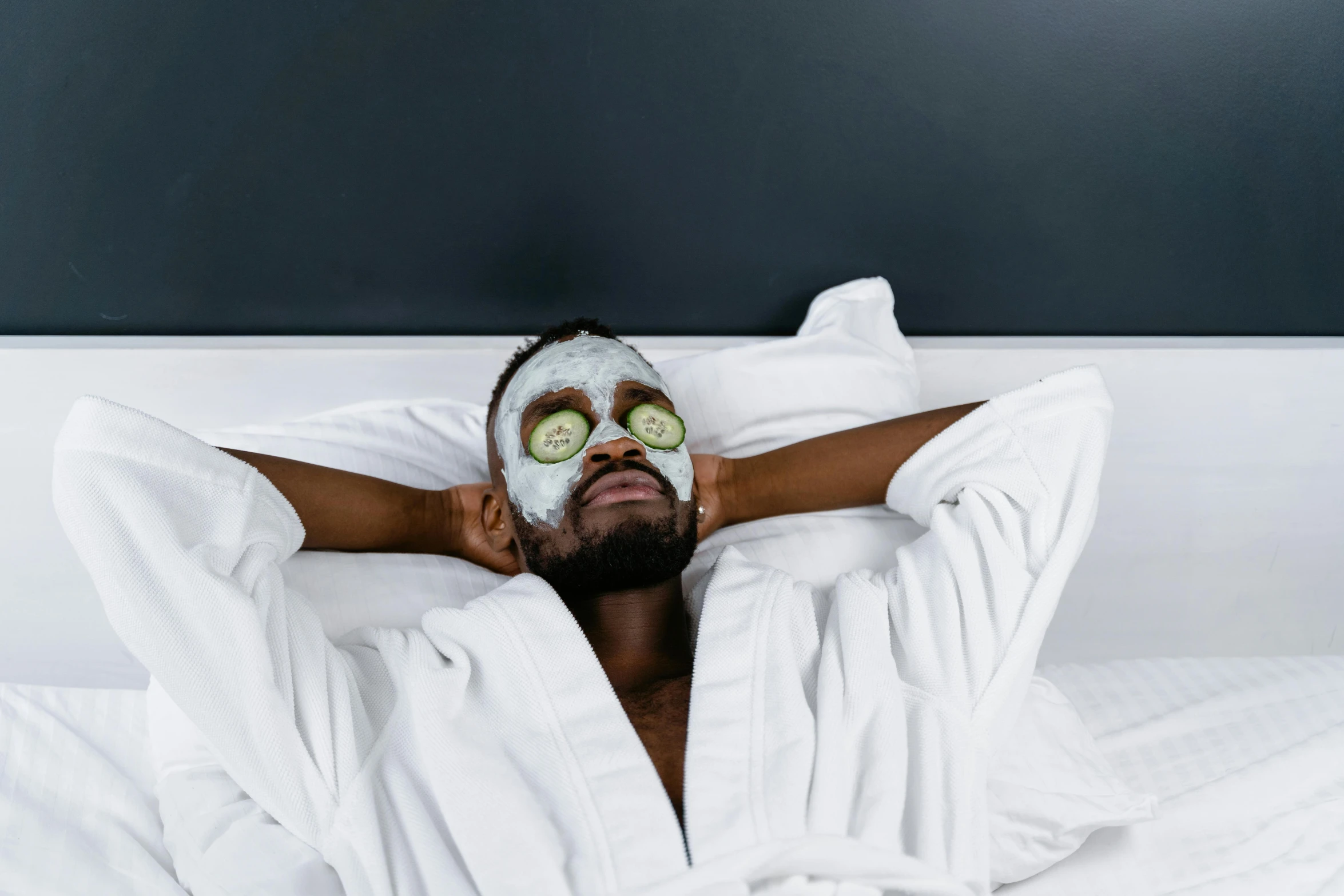 a man laying in bed with a mask on his face, trending on pexels, photoshoot for skincare brand, black face, holiday season, full-body