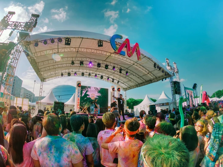 a group of people standing in front of a stage, a cartoon, by Simon Gaon, pexels contest winner, color field, wearing a tie-dye shirt, an outdoor festival stage, m & m mascot, view from the ground