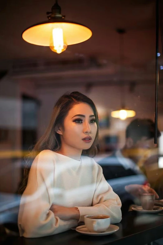 a woman sitting at a table with a cup of coffee, a portrait, inspired by Ruth Jên, pexels contest winner, beautiful young asian woman, sitting at a bar, reflecting, portrait”