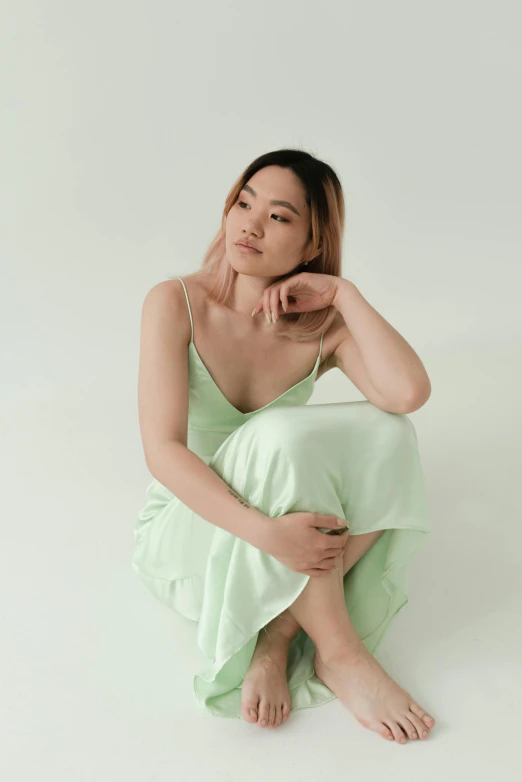 a woman sitting on the floor in a green dress, soft silk dress, leslie zhang, pastel hues, wearing a camisole