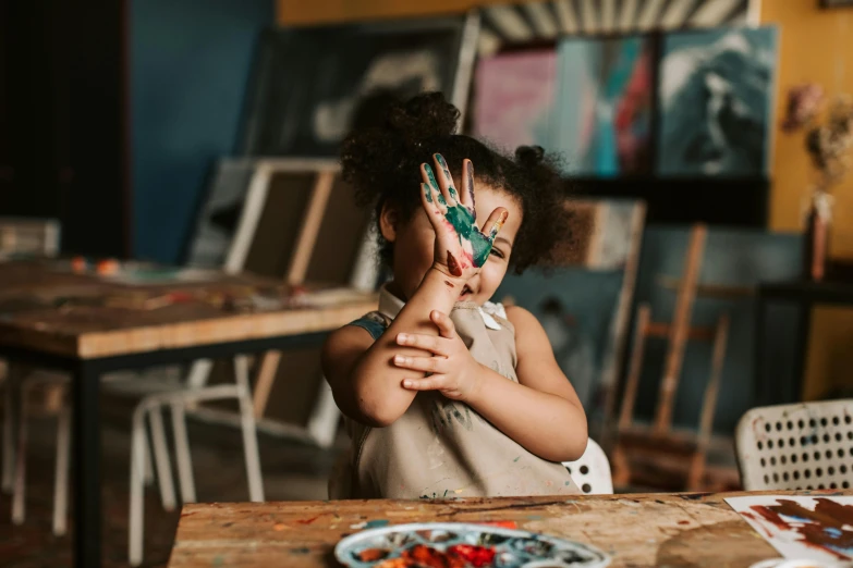 a little girl holding her hands up in front of her face, a child's drawing, by Arabella Rankin, pexels contest winner, model painting, hand on table, trending on pinterest，maximalist, painted overalls