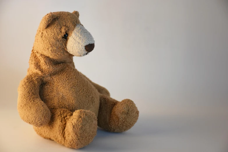 a brown teddy bear sitting on a white surface, sitting on the floor